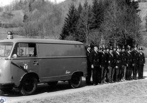 Die versammelte Mannschaft der Freiwilligen Feuerwehr Wembach mit dem ersten Fahrzeug vor dem Denkmal (1960er-Jahre)